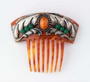  An intricately designed Art Nouveau hair comb with a semi-translucent amber-bodied base, topped with silver metalwork featuring a central orange cabochon and several smaller green cabochons.