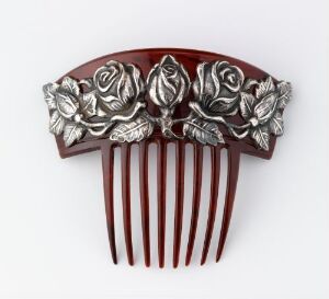  A decorative hair comb with a semi-circular, silver-toned metal top featuring intricately carved roses and leaves, atop rich mahogany brown teeth set against a light grey background.