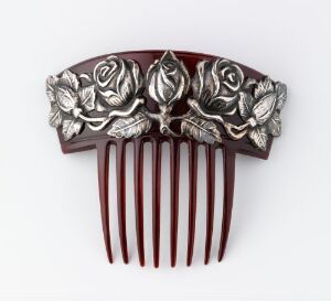  An ornamental hair comb with dark burgundy teeth and a decorative metallic top sculpted in the design of a bouquet of roses.