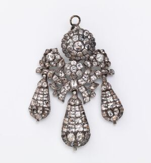  An ornate vintage pendant with a darkened silver-tone setting, featuring sparkling faceted stones set in a symmetrical pattern with a bow motif and hanging droplets, against a plain light background. Artist name and title are unknown.