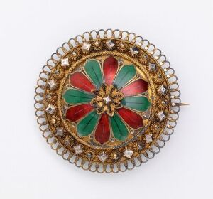  An intricate circular brooch with a gold filigree border and a central floral design featuring alternating ruby red and emerald green petals, set against a neutral white background.