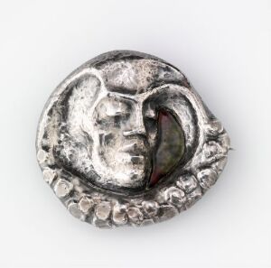  A circular silver medallion featuring a profile of a human face in relief, with a beaded edge. The surface shows varying shades of gray, indicative of a textured and slightly tarnished metal.