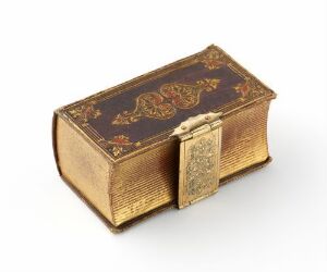  A small, antique golden box with an intricately etched texture and a maroon and gold floral design on the lid, featuring a detailed clasp. The box exhibits a luxurious, vintage charm.