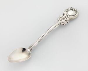  A lustrous silver spoon with an ornate handle featuring intricate swirls and a circular floral or sunburst motif, set against a pale background.