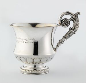  An antique silver cup with a decorative handle featuring a scroll design and a floral motif, also showing an engraved script on its shiny surface on a gray background. Artist's name and title are unknown.