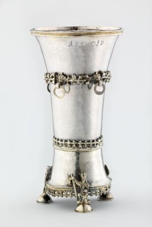  "Drikkebeger by Jørgen d.y. Bleckman, a decorative silver drinking vessel featuring engraved and punched designs with a girdle-like band around the center and an ornate, supportive base with stylized legs, demonstrating expert silverwork."