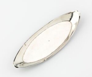  A polished metallic silver oval dish with tapered ends on a light gray background, reflecting light and showcasing a minimalistic design. Artistname and title are unknown.