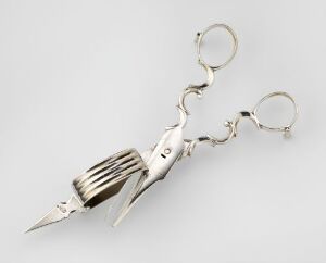  A silver, shiny hybrid utensil combining a pair of scissors on the top and a fork on the bottom, set against a light grey background.