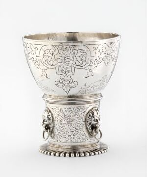  Silver drinking vessel "Drikkebeger" by Michel Plumeion, with intricate engravings and relief work, featuring a wide bowl on a decorated pedestal base with applied faces and beaded bottom edge.