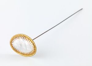  A gold-colored brooch with an oval mother-of-pearl inset on a white background, featuring a long straight pin for attachment to clothing.