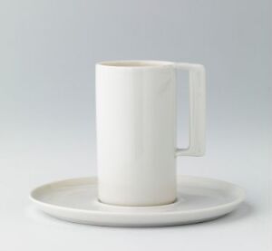  A white ceramic mug resting on a matching saucer with a light gray to white gradient background. The mug has a sleek, modern handle and a glossy finish.