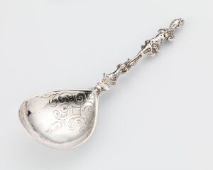  An antique silver spoon titled 'Skje' by an unidentified artist, featuring a detailed, engraved design with intricate patterns on both the bowl and handle, showcasing the reflective sheen of the silver material.