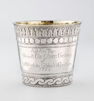  A beautifully crafted silver drinking beaker titled "Beger" by artist Peter Petersen, featuring chiseled and stamped designs with internal gilding, against a light grey backdrop.