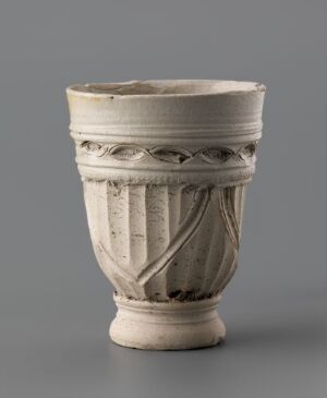  An off-white, historical ceramic vessel with a decorative band of intricately carved patterns resembling intertwined ribbons, set against a soft grey background.