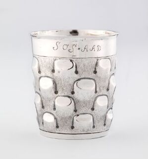  A silver cylindrical mug or container with an embossed pattern of overlapping circles and engraved text near the rim, on a plain neutral background. Artist name and title unknown.