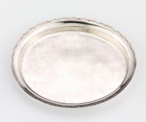  A round, silver or stainless steel shallow dish or plate with a reflective polished surface and a raised rim, set against a light grey background. The artist name and title are unknown.