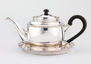  A shiny silver teapot with a dark handle on a matching silver saucer, placed against a light-colored background.