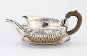  A polished silver teapot with Greek key patterns and a contrasting brown handle resting on a matching saucer against a light gray background.