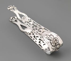  Silver sugar tongs "Sukkerklype" by artist Peter Petersen featuring repoussé and engraved designs with a partially pierced floral pattern, exemplifying fine silverwork with a polished metallic surface ranging from bright highlights to deep gray shadows.