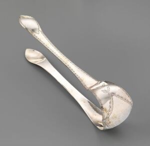  An antique silver sugar tongs with ornate engraving, displayed against a light grey background.