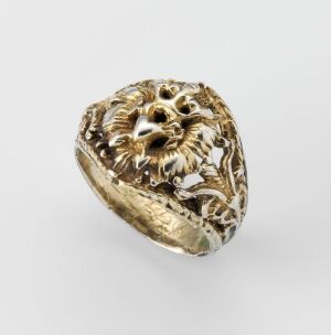  A gold-toned ring with an intricate lion's head design featuring detailed mane and expressive facial features, set against a plain light grey background.