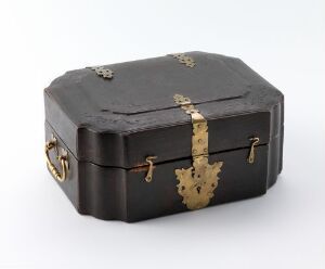  An antique octagonal box with a black polished surface and ornate gold metal accents including a latch, corner reinforcements, and side handles, set against a light grey background.