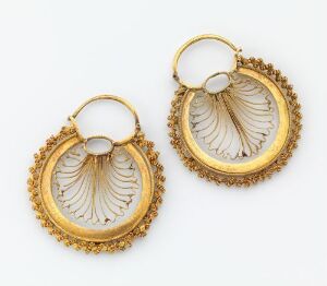  A pair of ornate golden earrings with a central milky white stone and a fan-shaped carving, set against a light background.