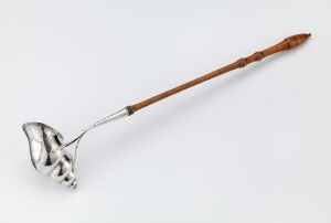  A decorative long-handled serving utensil with a carved wooden handle and a leaf-shaped, slotted metal bowl, set against a white background.