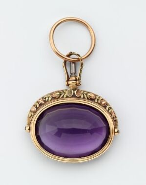  A golden pendant with a large, oval-shaped purple stone bordered by a decorative leaf motif, attached to a gold ring against a white background. Artist name and title are unknown.