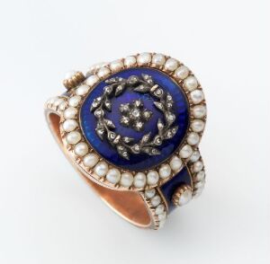  An elegant gold ring with a deep blue oval gemstone encircled by a halo of white pearls and smaller clear gemstones, set against a white background.