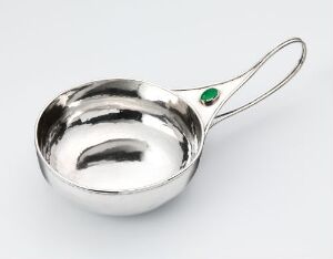  A polished silver saucepan with a long handle featuring an emerald green stone at the base of the handle, displayed on a neutral background.