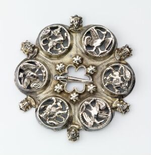  An intricate silver or pewter circular brooch or pendant with seven round elements, each featuring relief designs of animals or figures, likely of heraldic significance, against a light gray background. Artist name and title are unknown.