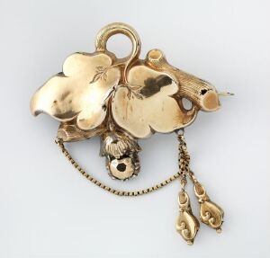 
 A golden floral brooch or pendant featuring a five-petalled flower with a smaller three-petalled flower attached by a chain and two tear-shaped pendants dangling from the bottom, all set against a light grey background.