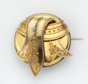  A golden circular brooch with detailed engravings and a pin at the back, set against a light gray background.