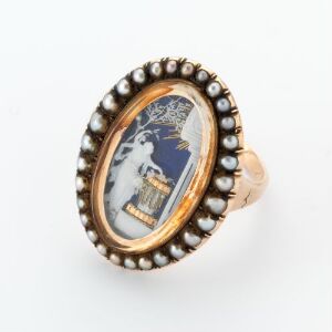  An oval-shaped ring with a gold band and pearl border showcasing an intricate miniature scene with a central white figure against a dark background with gold accents.