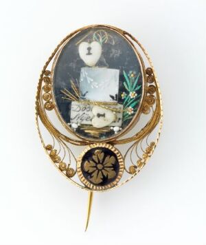  An antique oval-shaped brooch with an ornate gold frame featuring a miniature scene with symbolic elements such as a classical bust, the word "DEATH" on a paper, a willow and cypress tree, a bone, and a white owl carrying a scroll against a dark background.