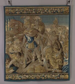  A tapestry depicting a Medieval or Renaissance scene with a central warrior figure on a rearing horse surrounded by other riders and horses, in muted earthy tones with a detailed, lighter decorative border at the top.