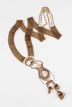  A traditional brown-toned necklace with a ribbon-like top and a central circular pendant, featuring symmetrical patterns and fringe details against a white background.