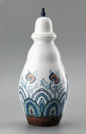  A decorative feldspar porcelain bottle with a white glaze and underglaze blue, green, and brown decorations in a stylized plant-like pattern, designed by Hans Flygenring. The bottle has a rounded base, a slender neck, and a topped blue knob on the lid.