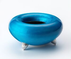  A blue glossy ceramic-like object with a donut shape on three metallic claw-foot stands against a white background.