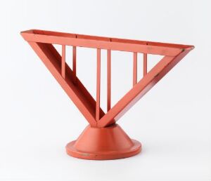  A welded and lacquered metal container by artist Marianne Brandt, featuring a geometric design with an inverted cone shape made from vertical metal bars on a circular base, all uniformly painted in a gloss reddish-orange color.