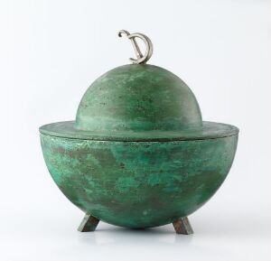  Antique bronze bowl with a lid shaped like an apple, sitting on three small feet, with a green patina finish and a stem-like golden handle on top, against a white background.