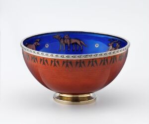  A decorative bowl with a terracotta body and a cobalt blue rim featuring gold or bronze animal figures and round dots, with a Greek key design beneath and a metallic gold base, set against a neutral background.