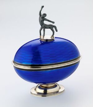  A decorative spherical container in cobalt blue with a golden equatorial stripe and circular base, adorned with a silver figurine on top, alluding to opulence and artistry.