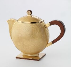  A spherical golden-colored metallic teapot with a wooden handle and a ribbed texture near the top, standing against a neutral white background.