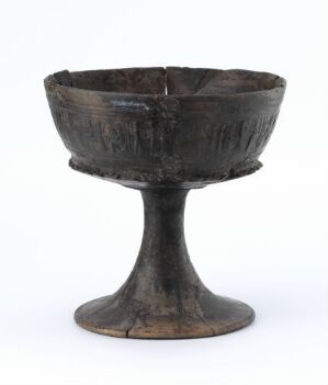  An old, dark brown chalice with a textured surface and irregular rim, resembling aged bronze, on a plain off-white background.