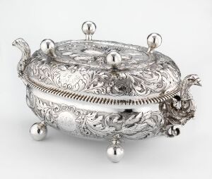  An ornate silver tureen ("Terrin") with intricate engravings and raised decorations, reflecting light to show shades of gray. Artist Jens Hansen Børring skillfully combines hammered, cast, and soldered techniques for an exquisite finish in this piece of tableware.