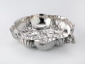  An intricately designed silver butter dish titled "Smørskål" by Baard Gandolphi Bonsach, featuring chased and punched designs with engraved details and cast handles, showcasing the gleaming craftsmanship of drevet og punslet sølv on a gray background.