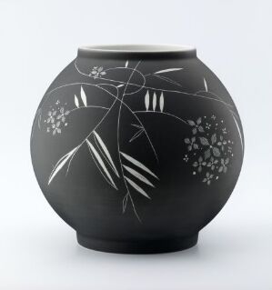  A black matte vase with silver-gray botanical etchings, featuring slender stems, leaves, and flower clusters, against a white background.