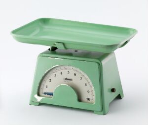  A vintage mechanical kitchen scale with a pastel-mint green body and a slightly darker shade weigh platform, featuring an off-white semi-circular dial with black numbering, set against a neutral background.